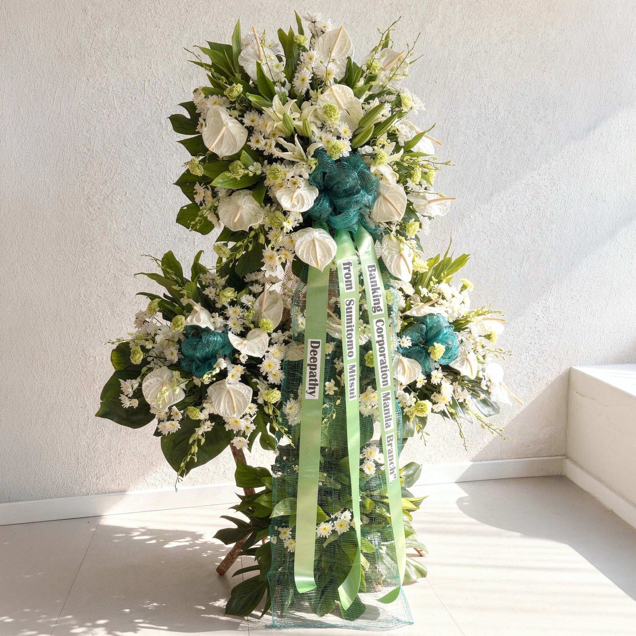 White funeral standing arrangement with anthurium lilies orchids mums and green foliage elegant sympathy floral tribute for memorial and condolence services