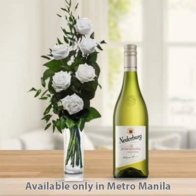 6 white roses arranged with greens in vase and bottle of white wine